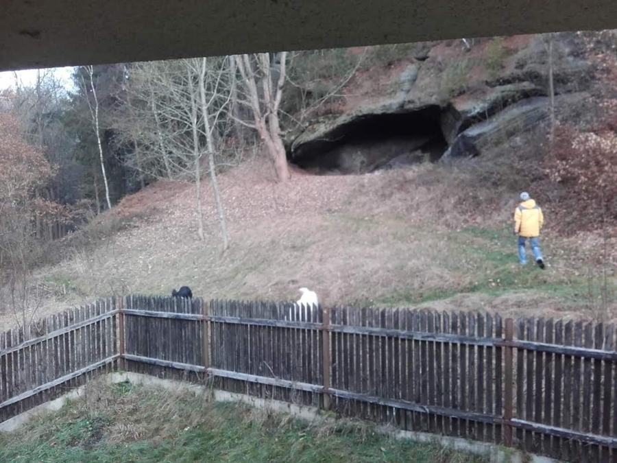 Laťkový plot zahrady a za ním pískovcová skála s jeskyní